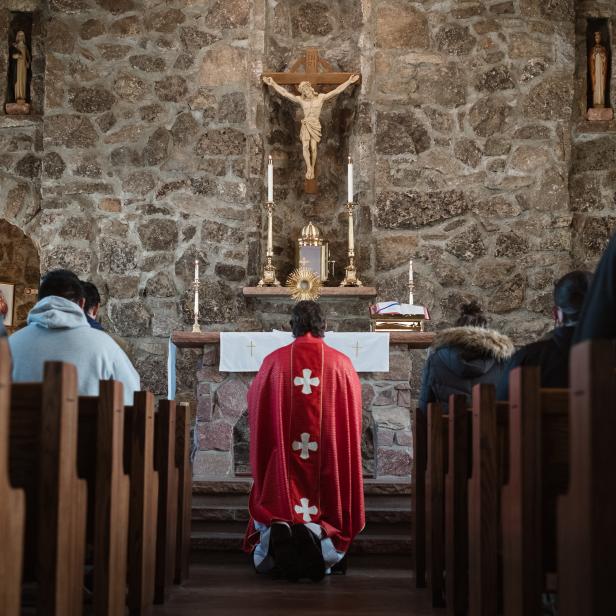 Ein Priester kniet vor dem Altar in einer Kirche, umgeben von Gläubigen.