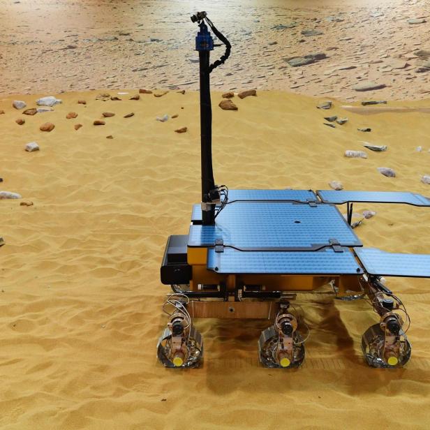 Ein Rover steht auf einer sandigen, steinigen Oberfläche, möglicherweise auf dem Mars.