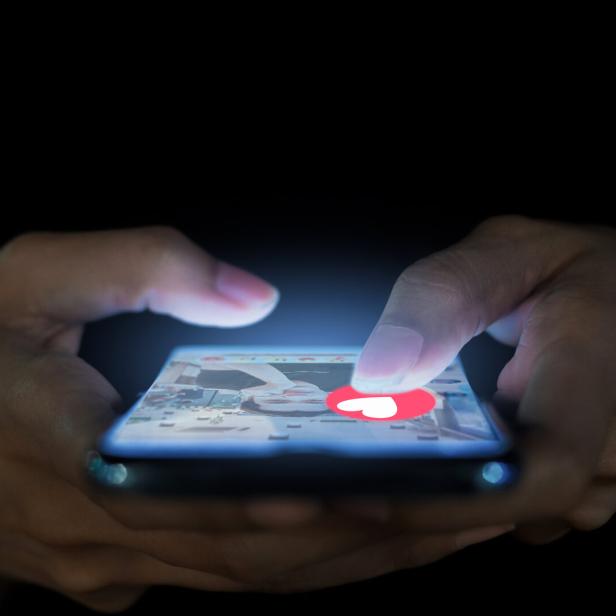 Eine Person tippt auf ein Smartphone mit einem roten Herz-Symbol auf dem Bildschirm.