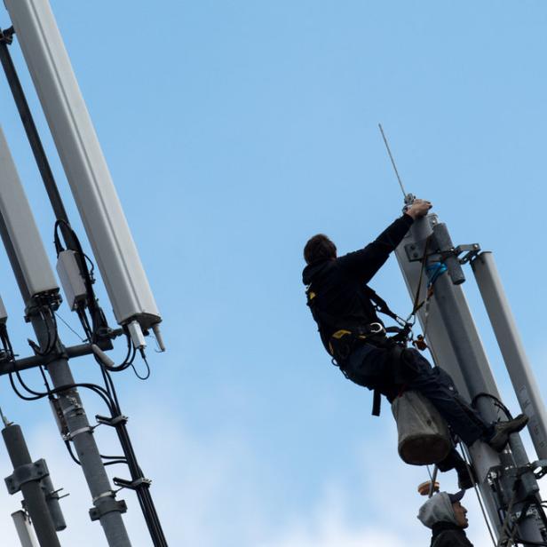 Ein Arbeiter klettert auf einen Mobilfunkmast vor blauem Himmel.
