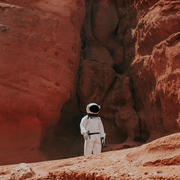 Ein Astronaut steht vor einer roten Felsformation.