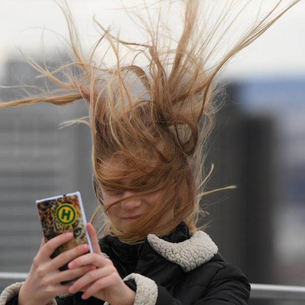 Frau nimmt Selfie von sich mit vom Wind zerzausten langen Haaren auf