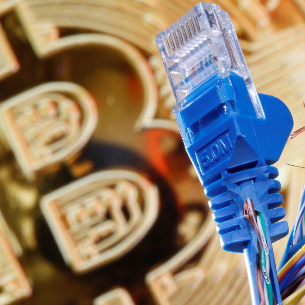 Broken Ethernet cables are seen in front of a displayed representation of the bitcoin network in this illustration