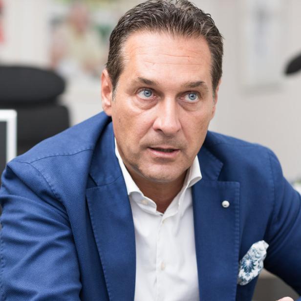 Ein Mann in einem blauen Sakko sitzt an einem Schreibtisch.