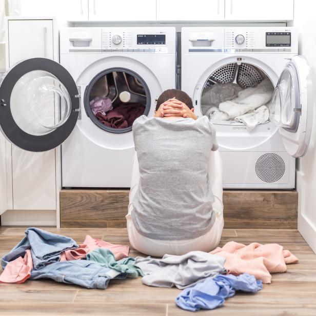 Young Tired sad Woman sitting on the floor in laundry room, back view