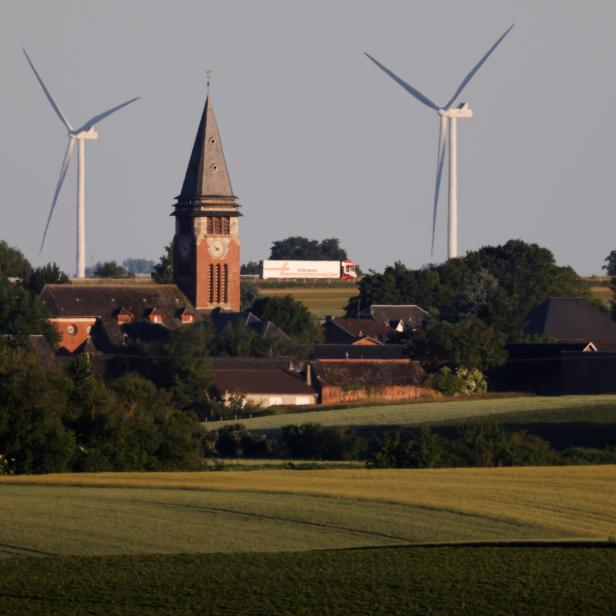 Two power-generating windmill turbines are seen behind the church of the village in Ruyaulcourt