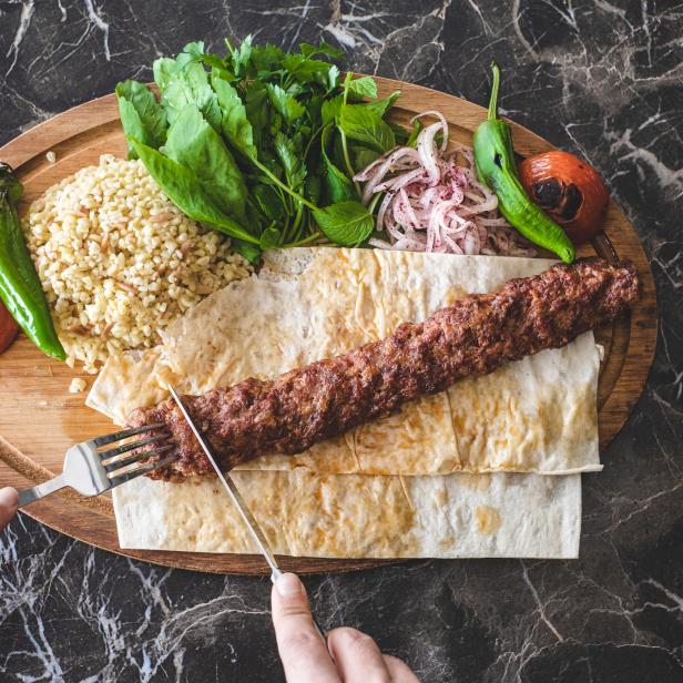 Ein Adana-Kebab wird mit Beilagen auf einem Holzteller serviert.