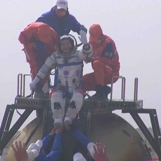 Ein chinesischer Astronaut sitzt auf einer Raumkapsel und winkt.