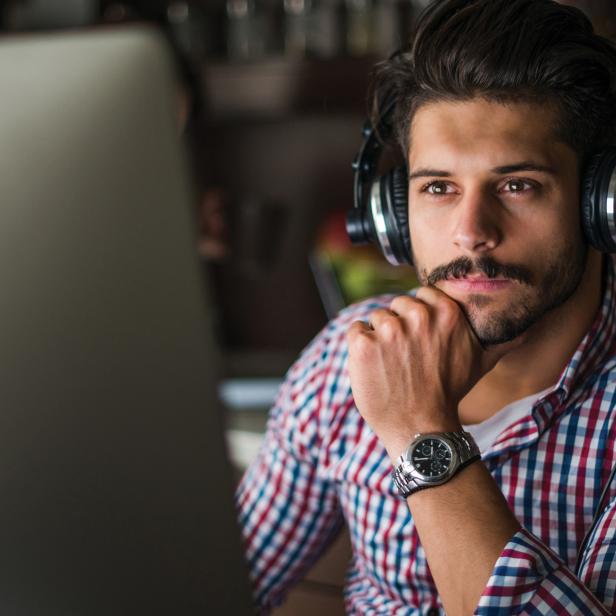 Ein Mann mit Kopfhörern sitzt vor einem Computer und denkt nach.