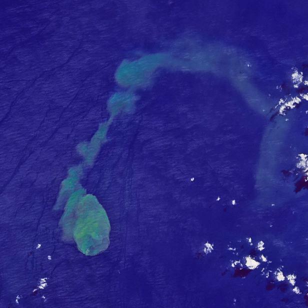 Satellitenansicht einer Insel mit einer Wolke aus vulkanischem Material im Ozean.
