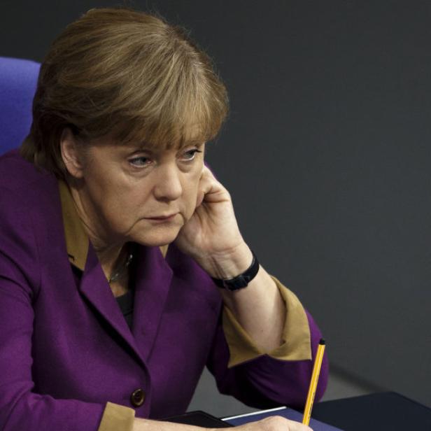 Angela Merkel sitzt nachdenklich mit einem Stift in der Hand.