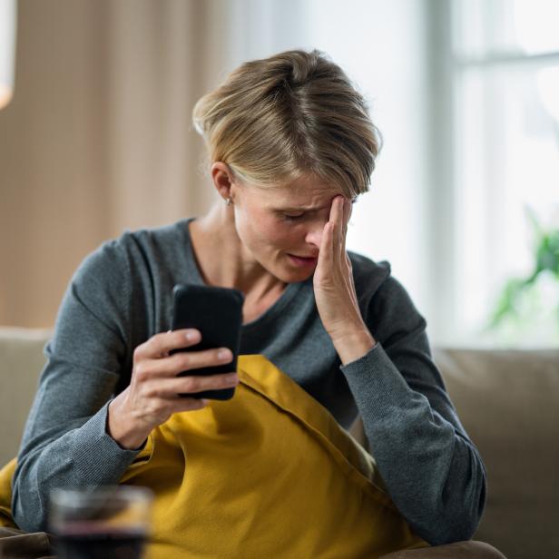 Woman with smartphone indoors on sofa at home feeling stressed, mental health concept.