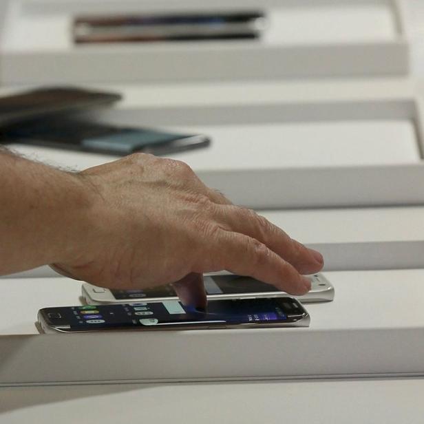 Eine Hand berührt den Bildschirm eines Smartphones in einer weißen Auslage.