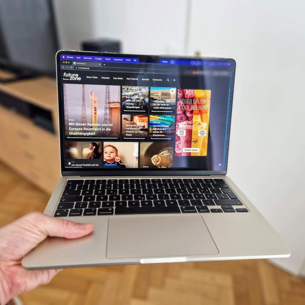 Ein MacBook wird in der Hand gehalten und zeigt die Webseite futurezone.at.