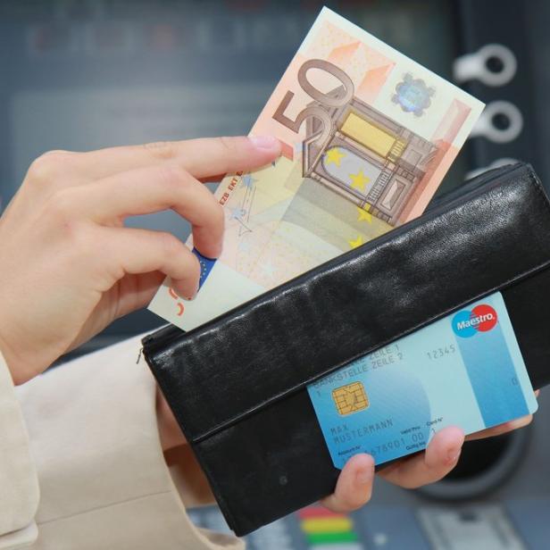 Eine Person entnimmt mit einer Geldbörse und einer Maestro-Karte 50 Euro an einem Geldautomaten.