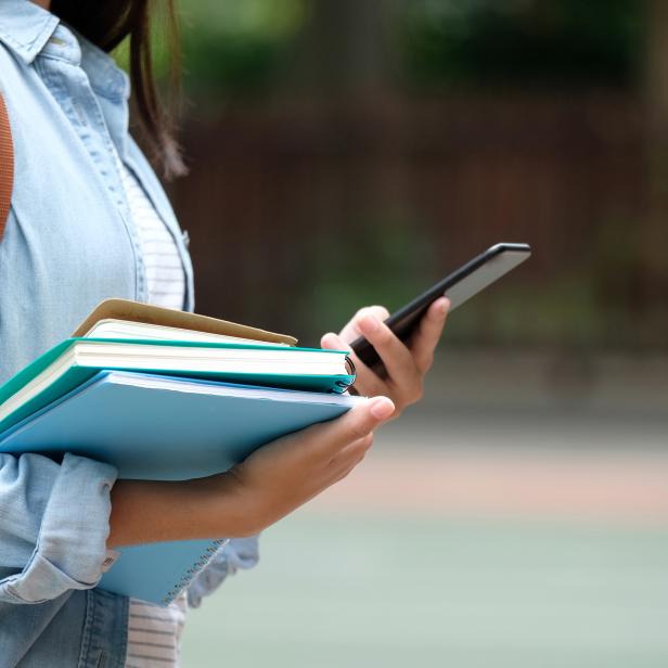 Student girl holding books and smartphone while walking in school campus background, education, back to school concept
