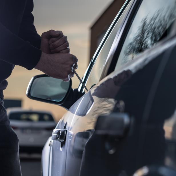 Auto thief in black balaclava trying to break into car