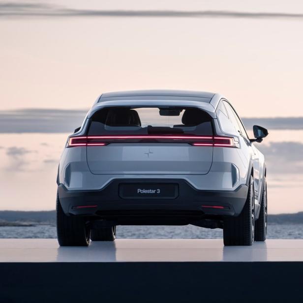 Die Rückansicht eines silbernen Polestar 3 vor einer Küstenlandschaft.