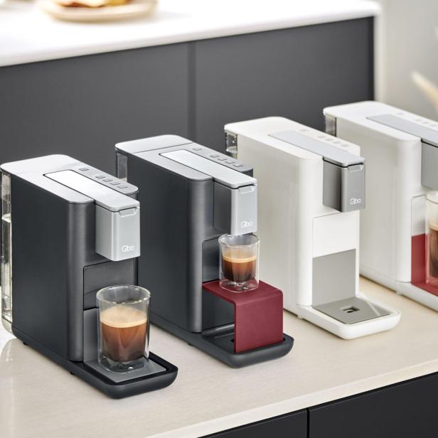 Drei Qbo-Kaffeemaschinen in verschiedenen Farben stehen auf einer Küchentheke.