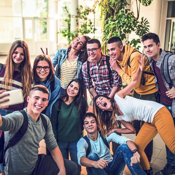 Large group of happy students taking a selfie with cell phone at school.