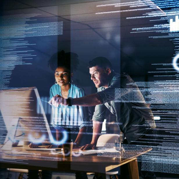 Zwei Personen arbeiten gemeinsam an einem Computer mit Codeanzeige.