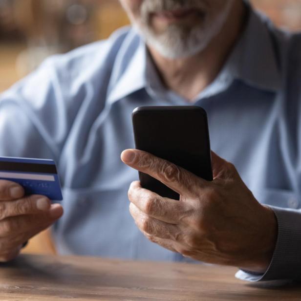 Close up mature man using phone, holding plastic credit card