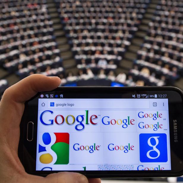 Eine Hand hält ein Smartphone mit einer Google-Logosuche vor einem Publikum.