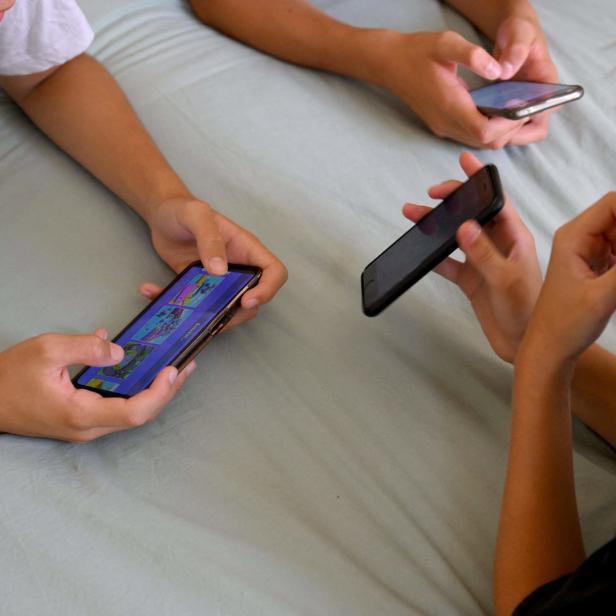 Drei Jugendliche liegen auf einem Bett und benutzen ihre Smartphones.