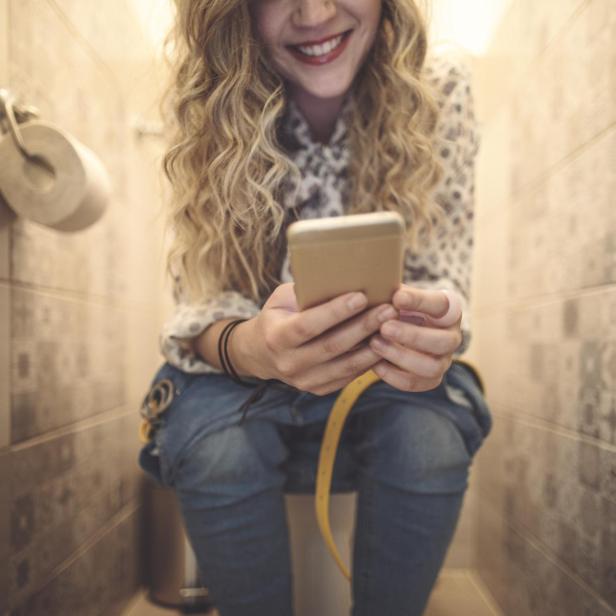 Frau auf der Toilette mit Handy