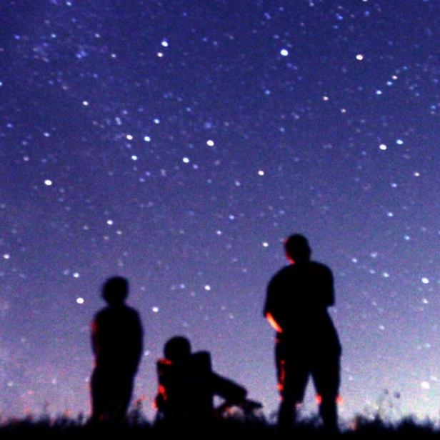 Drei Personen betrachten den Sternenhimmel.