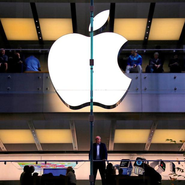 FILE PHOTO: A customer stands underneath an illuminated Apple logo as he looks out the window of the Apple store located in central Sydney