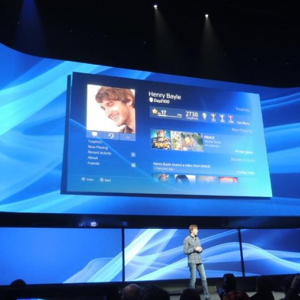 Ein Mann präsentiert die PlayStation-Benutzeroberfläche auf einer großen Leinwand.