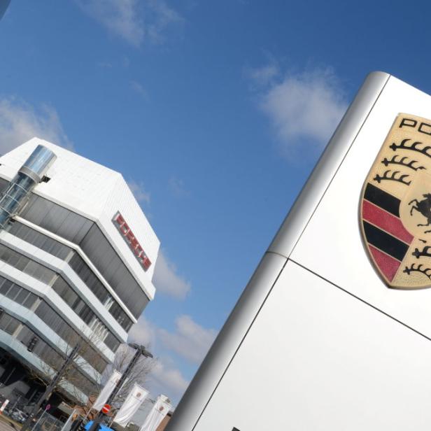 Das Porsche-Logo vor einem modernen Bürogebäude unter blauem Himmel.