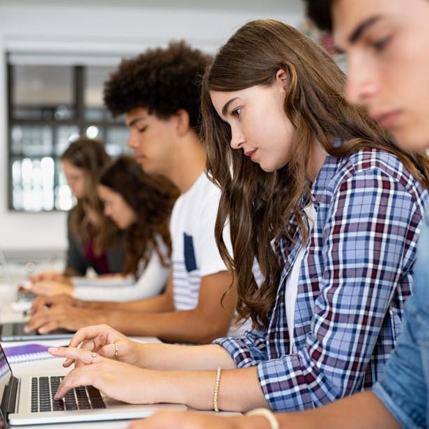 Group of high school students using laptop in classroom