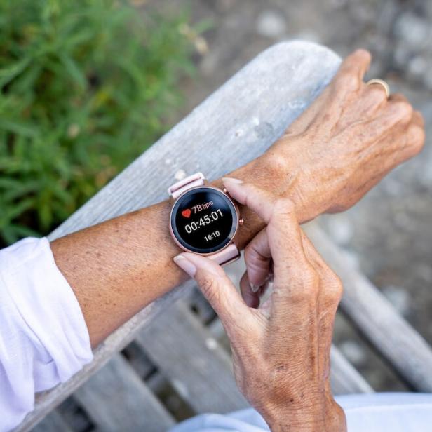 Eine ältere Frau überprüft ihre Herzfrequenz und Trainingszeit auf einer Smartwatch.