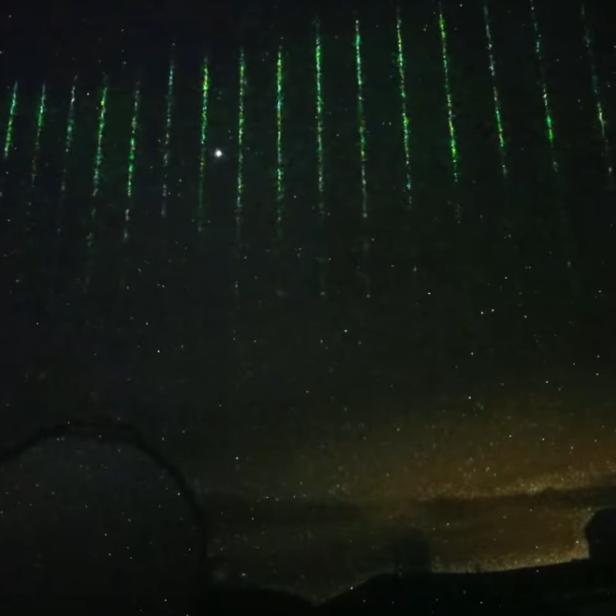 Laserstrahlen von einem Satellit am Nachthimmel über dem Subaru Teleskop auf Hawaii