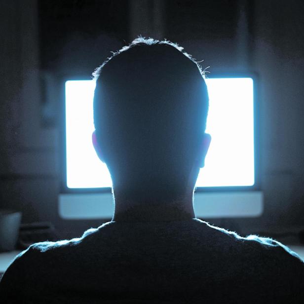 Man seated in front of computer monitor at night