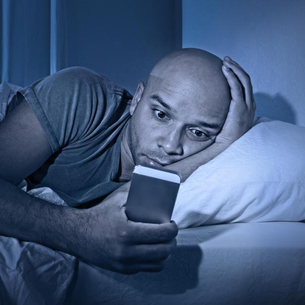 young cell phone addict man in bed using smartphone