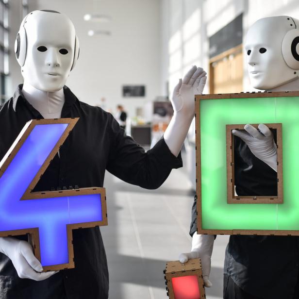 Zwei Personen mit Robotermasken halten leuchtende Zahlen, eine blaue Vier und eine grüne Null.