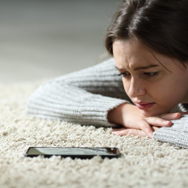 Symbolbild: Teenager blickt traurig auf das Smartphone.