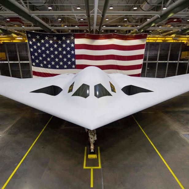 Ein B-21 Raider Tarnkappenbomber steht vor einer großen US-Flagge.