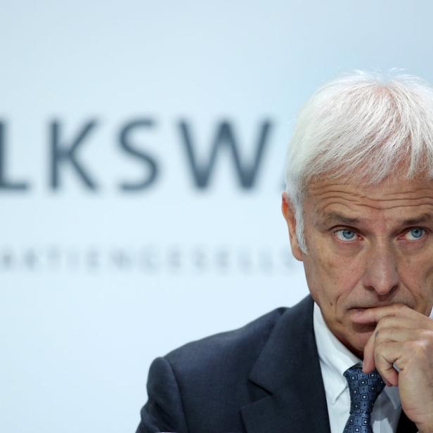 Ein Mann mit weißem Haar und Anzug vor einem Volkswagen-Logo wirkt nachdenklich.