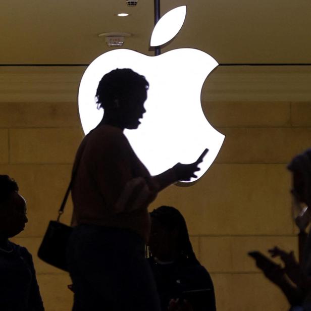 women uses her iPhone mobile device as she passes a lighted Apple logo at the Apple store in New York