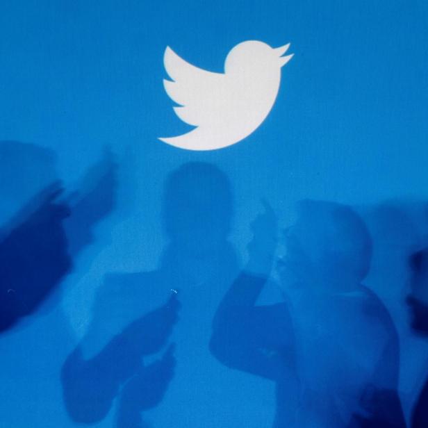 FILE PHOTO: Shadows of people holding mobile phones are cast onto a backdrop projected with the Twitter logo  in Warsaw