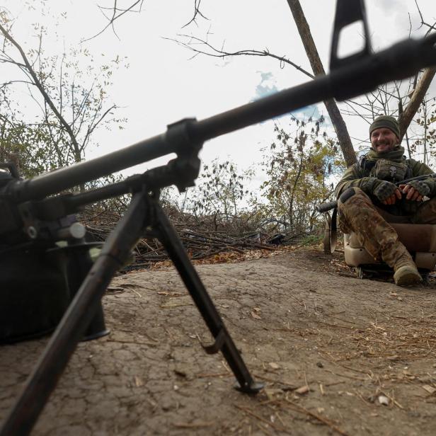 Ukrainian serviceman Yuriy smiles next to a machine gun at a position on a frontline in Mykolaiv region