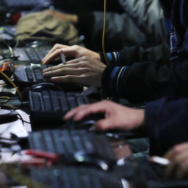Mehrere Personen sitzen an Computern, eine raucht eine Zigarette.