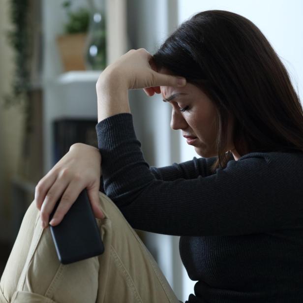 Sad woman holding smart phone complaining at home