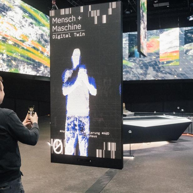 Ein Mann fotografiert eine Ausstellung mit dem Titel „Mensch + Maschine Digital Twin“.