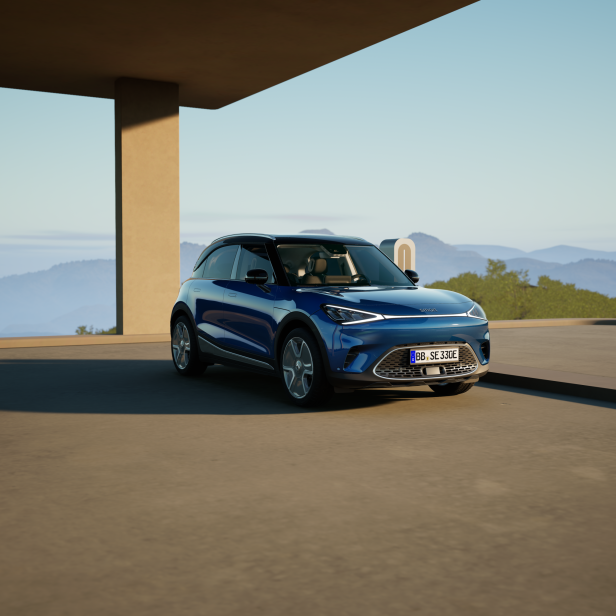Ein blauer Smart steht vor einer modernen Ladestation mit Bergpanorama.