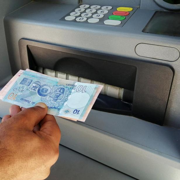 FILE PHOTO: A man displays Tunisian dinar banknotes after withdrawing cash from an ATM machine in Tunis